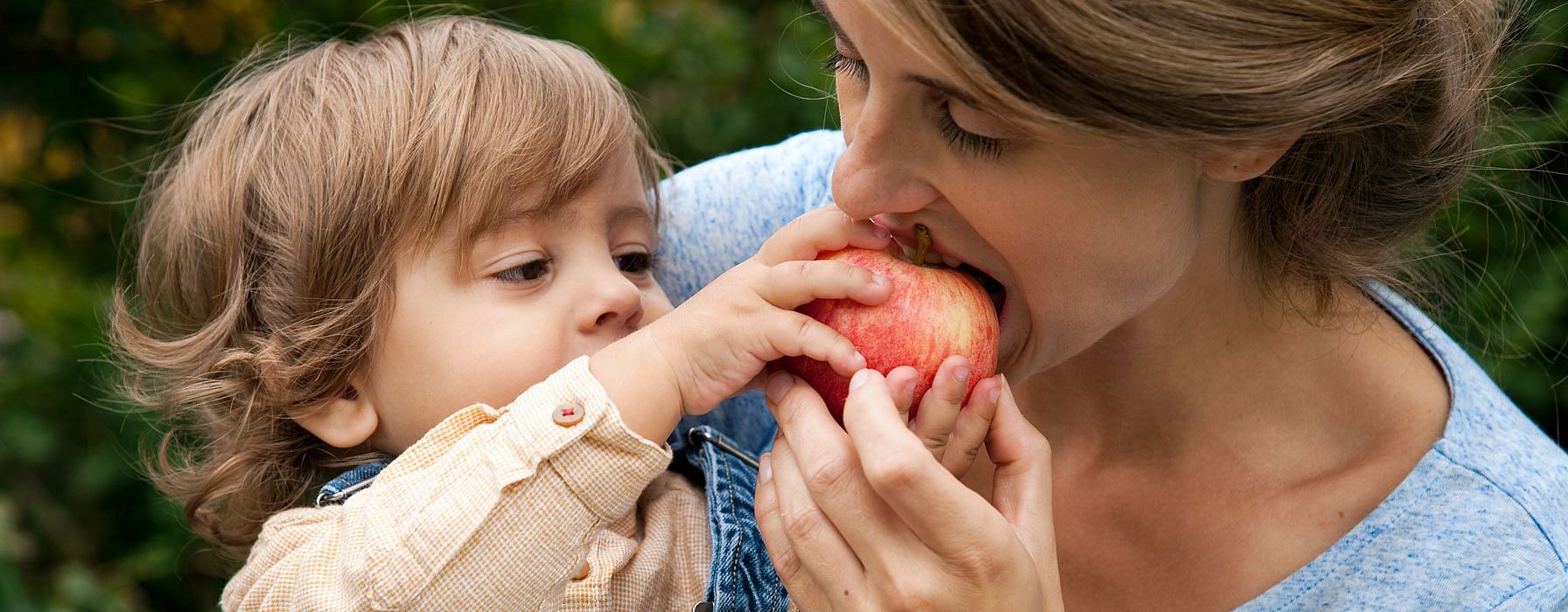 Mujer mordiendo una manzana que le da un niño pequeño que tiene cogido en brazos