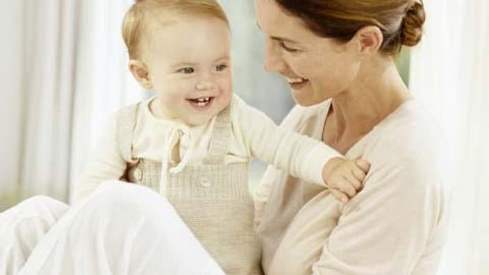 mujer sonriendo al bebé que tiene en brazos
