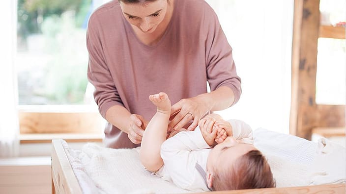 madre sonriendo cambiando pañal a bebé tumbado