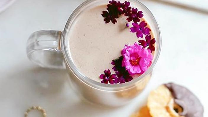 mesa donde se ve un vaso con infusión, decorado con flores, dos pastas y productos de cuidado facial de Weleda