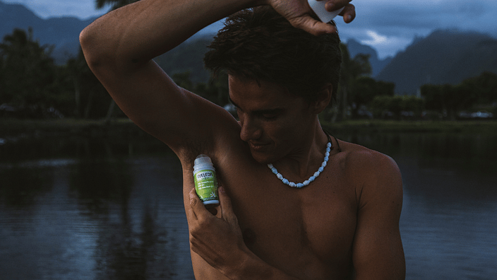 hombre aplicandose desodorante roll-on de weleda en mitad de la naturaleza, con un lago de fondo