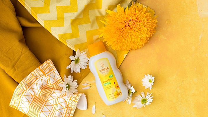 aceite corporal de bebé de calendula al lado de una flor de calendula