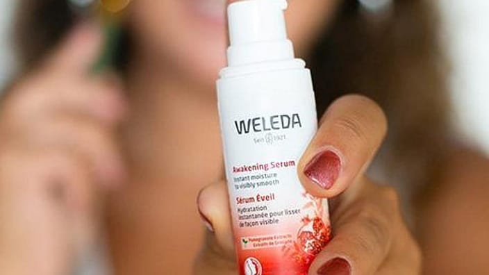 mujer con un bote de crema de granada de weleda