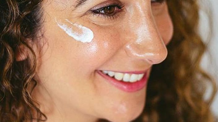 mujer soriendo echandose crema en la cara