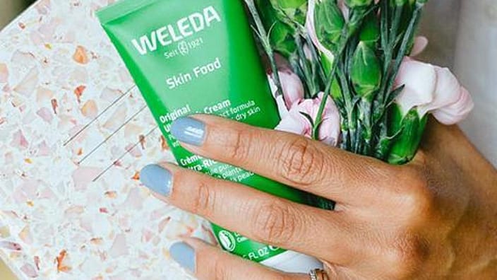 mano de mujer con skin food de weleda y flores