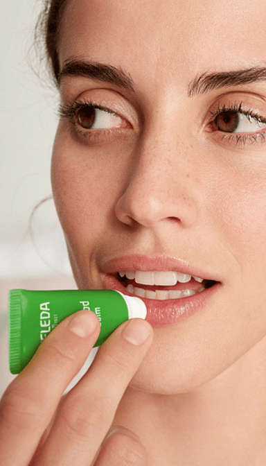 mujer aplicandose el lip balm skin food de weleda