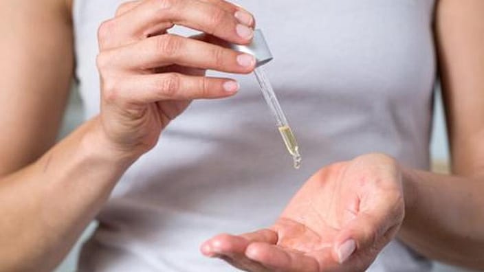 mujer echando gotas de aceite facial reafirmante en una mano