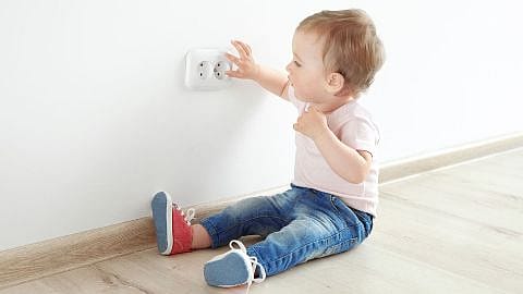 Niño pequeño sentado en el suelo jugando con el enchufe de una casa