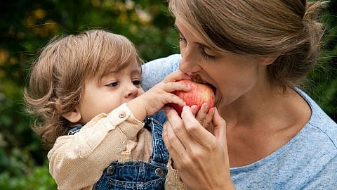 Mujer mordiendo una manzana que le da un niño pequeño que tiene cogido en brazos