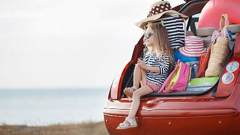niña sentada en el maletero lleno de maletas