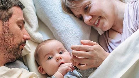 bebe tumbado en la cama con sus padres
