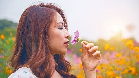 mujer en el campo oliendo una flor